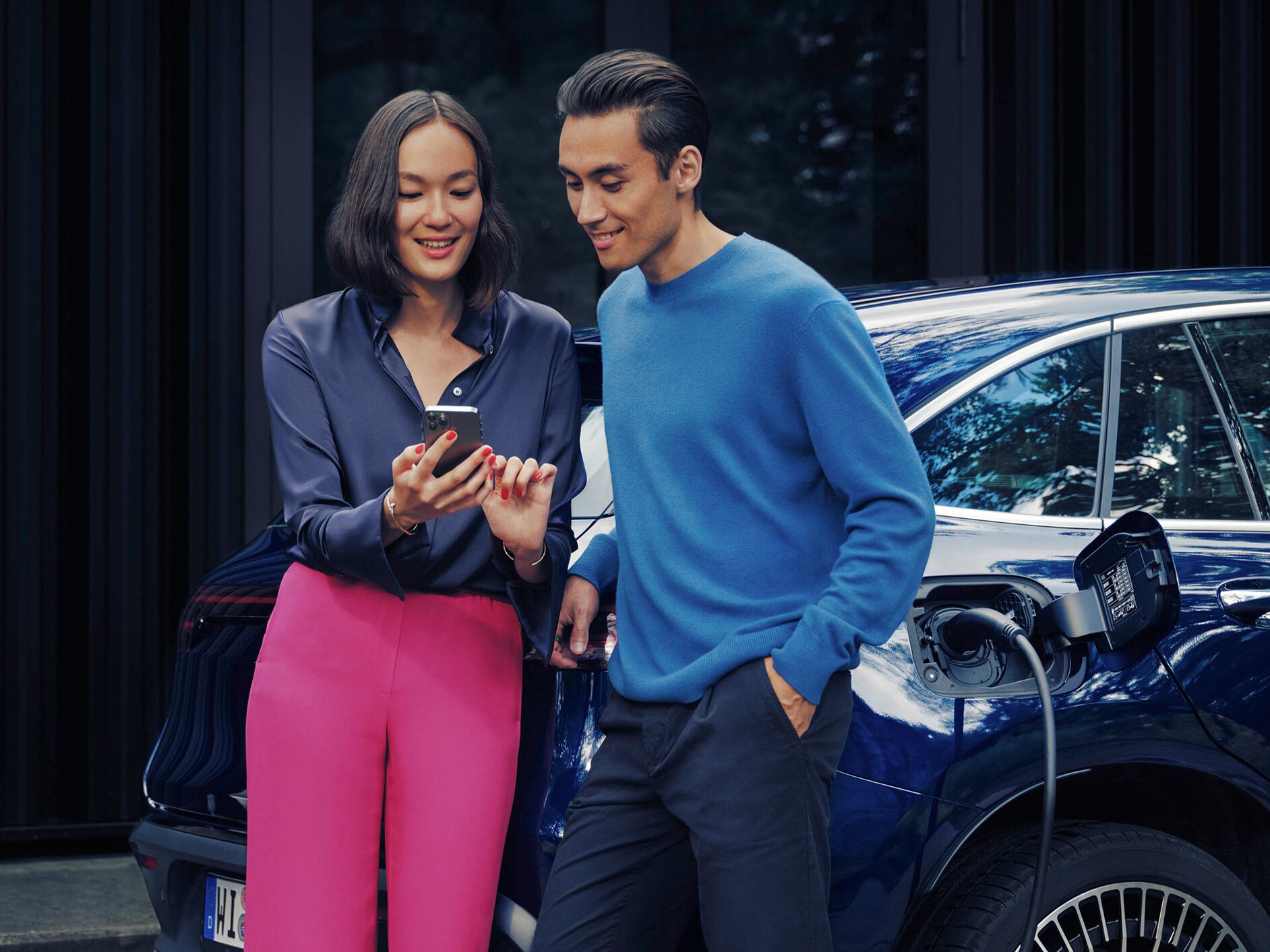 Man and woman looking at a phone together next to blue Mercedes-Benz EQC