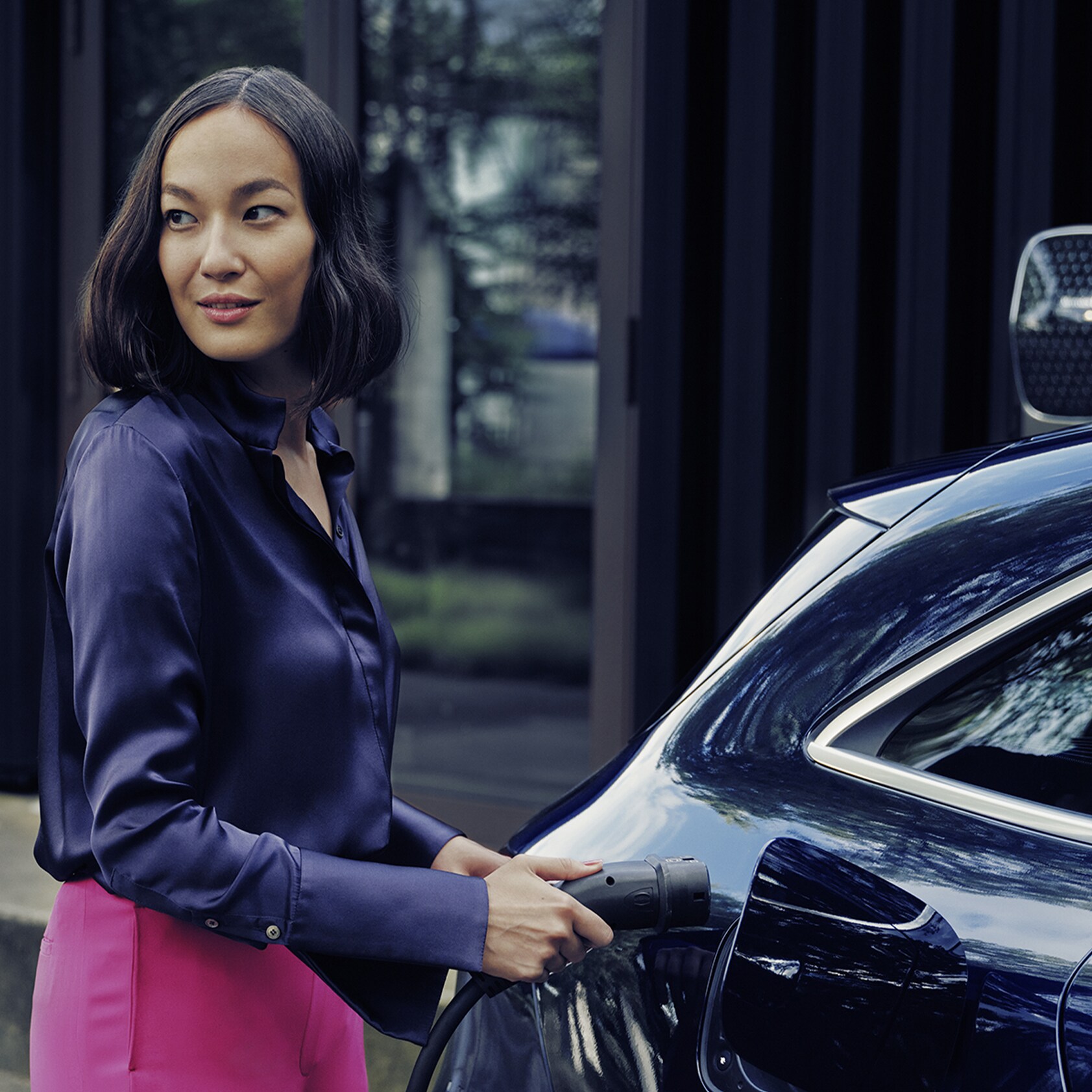 A woman with a smartphone standing in front of a Mercedes-Benz Wallbox charging a Mercedes-Benz electric car.