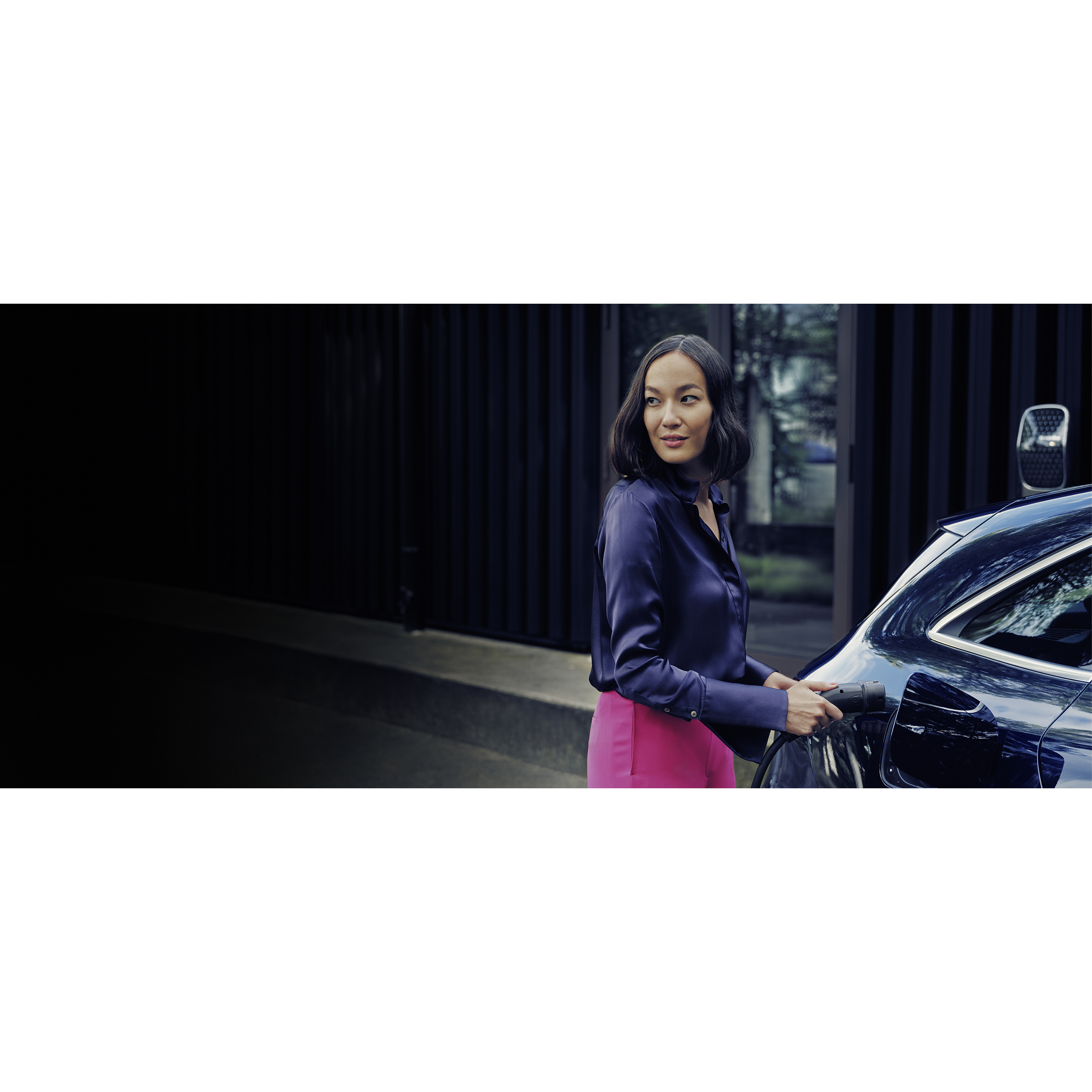 Charging at home | Mercedes-Benz A woman with a smartphone standing in front of a Mercedes-Benz Wallbox charging a Mercedes-Benz electric car.
