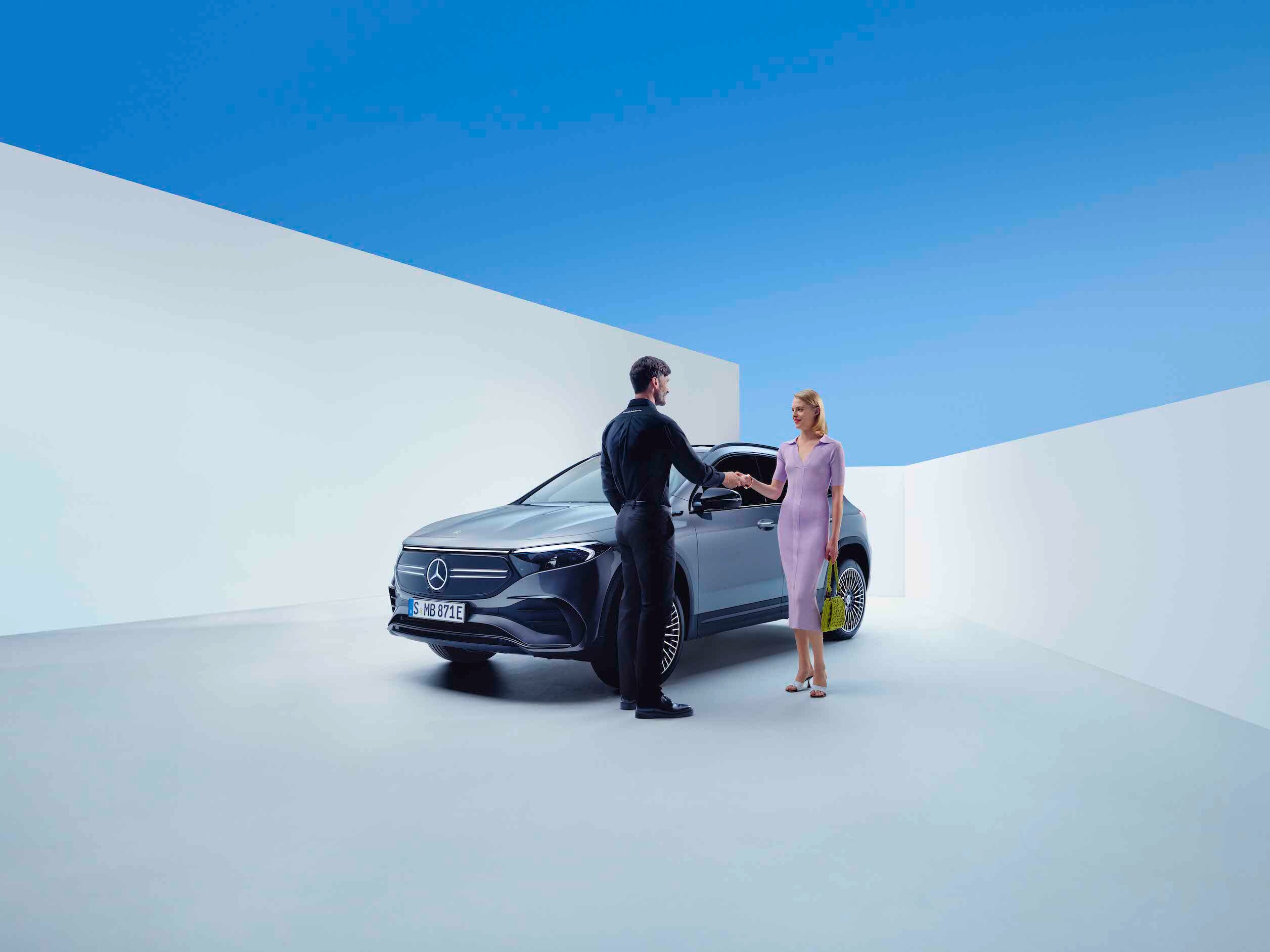 A man and a woman shake hands in front of a Mercedes-Benz.