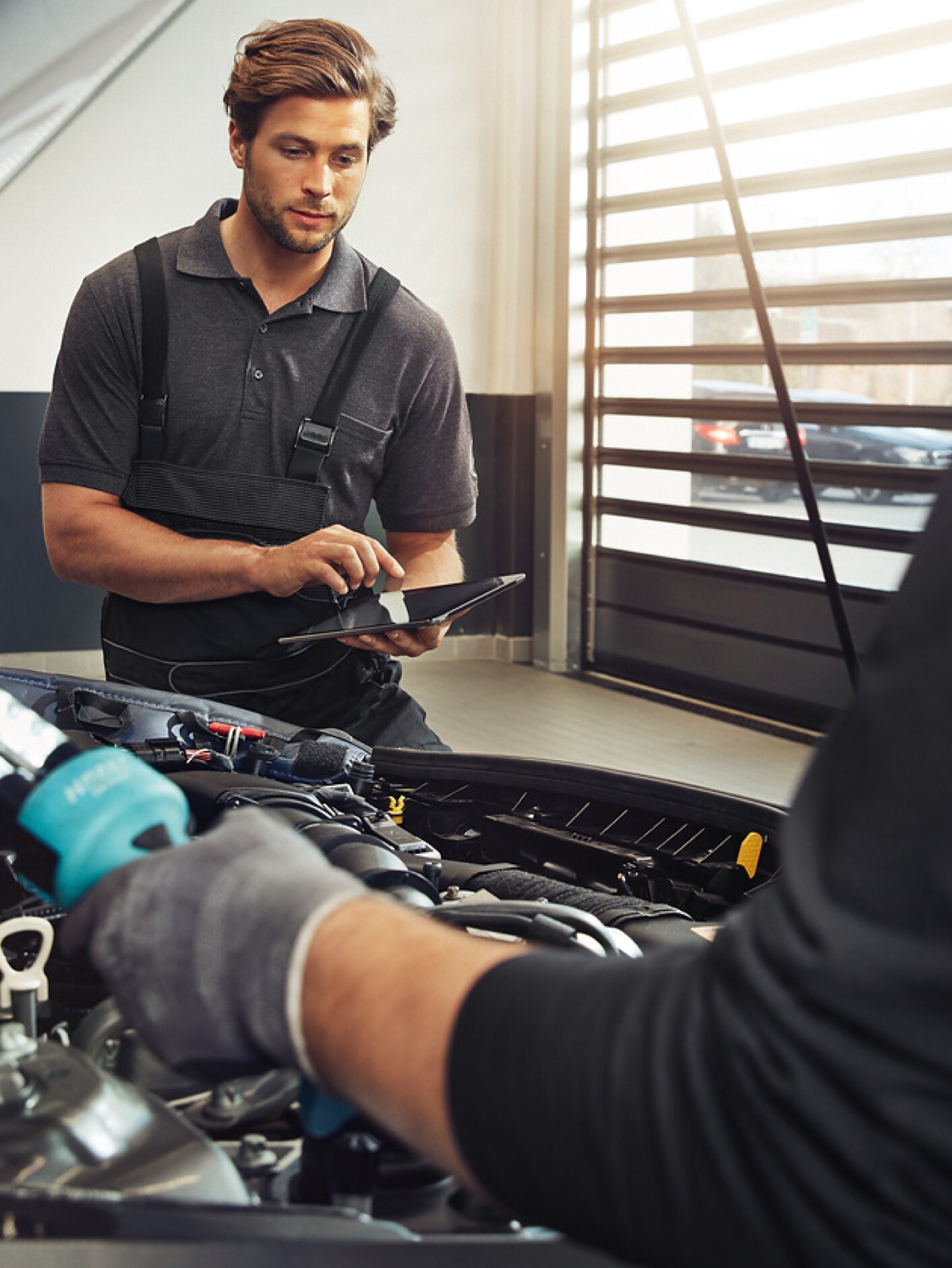 Two Mercedes-Benz technicians check the engine compartment of a vehicle.