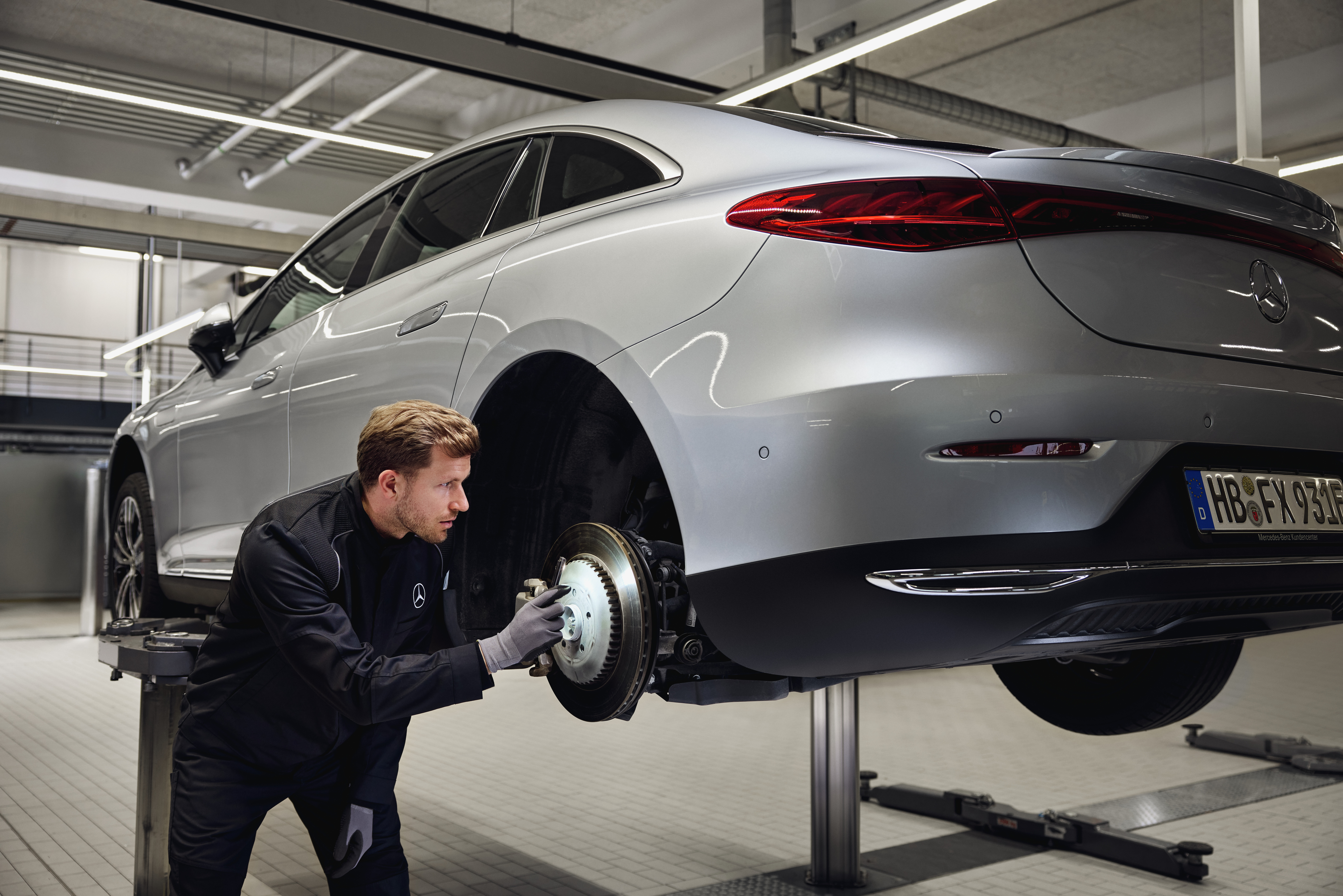 Mercedes‑Benz Genuine Brake Replacement Mercedes‑Benz vehicle raised on a lift with a technician inspecting the rear brake system for a replacement of genuine parts service.