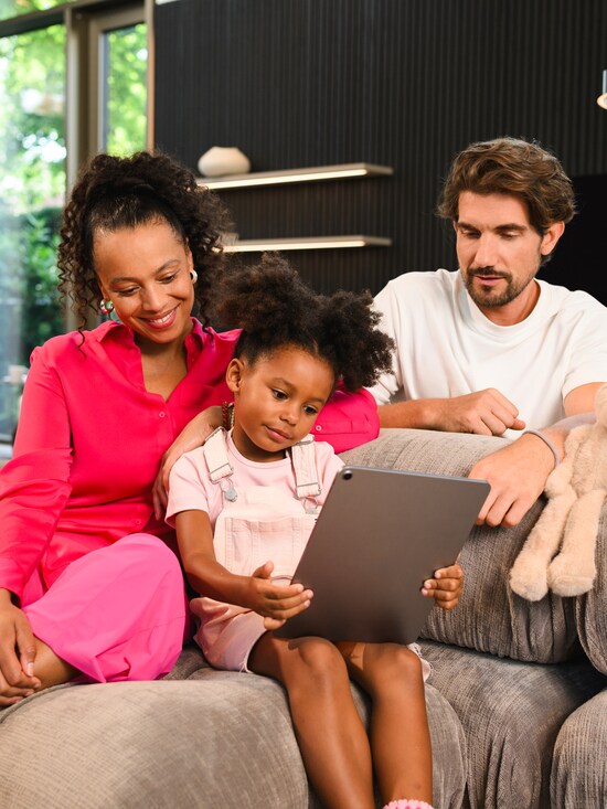 A family sitting on the couch looking at a tablet in the little girls hands