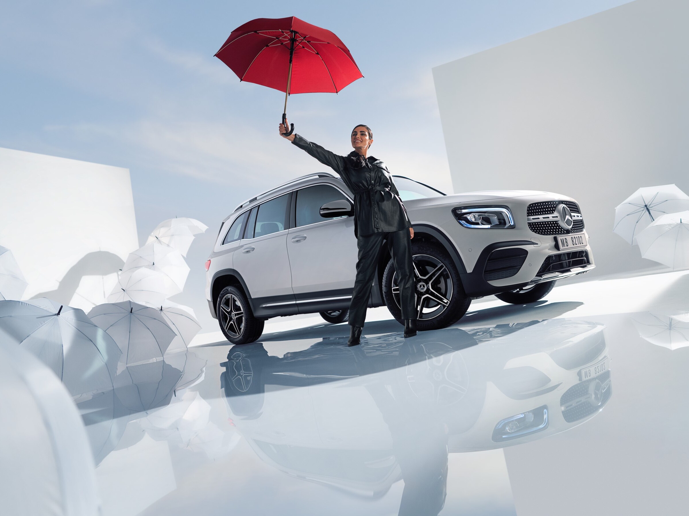 A woman is standing beside a Mercedes-Benz with white umbrellas around the floor