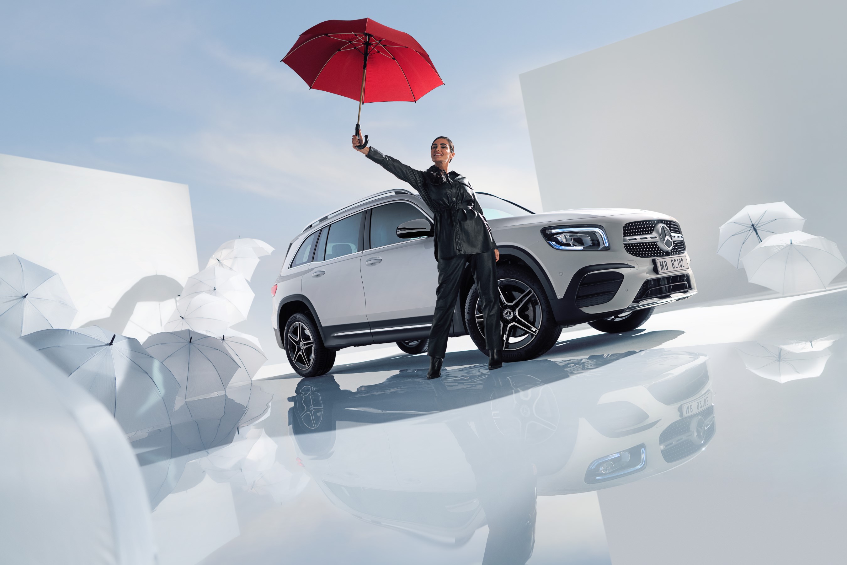 Have a safe journey with the Mercedes-Benz warranty for new vehicles. | Mercedes-Benz A woman is standing beside a Mercedes-Benz with white umbrellas around the floor
