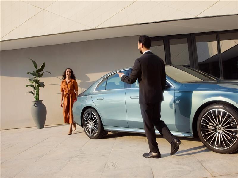 A man leans against a wall next to a Mercedes-Benz.